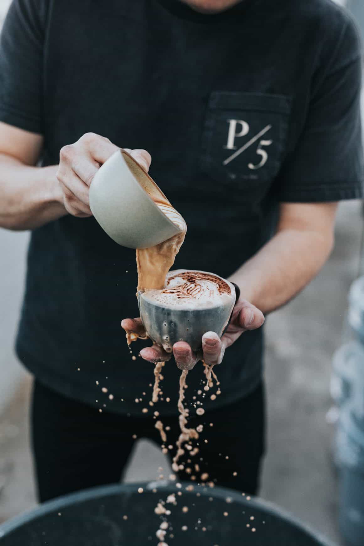 A guy holding an overflowing cup of coffee